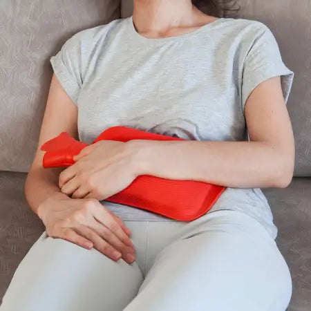 Lifestyle image of woman using a heating pad for PMS cramp relief and menstrual discomfort